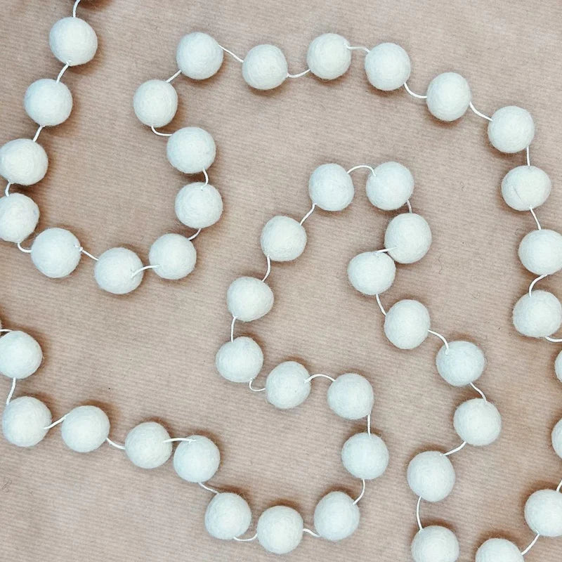 Guirlande décorative New Heidi composée de billes en laine feutrée blanche sur ficelle naturelle.