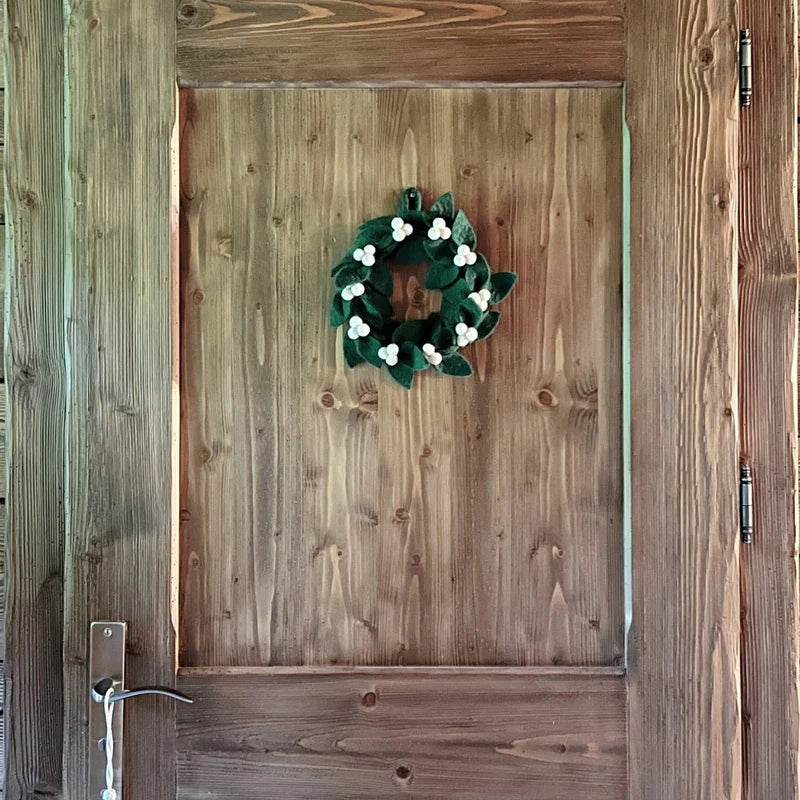 Grande couronne décorative gui et houx en feutrine installée sur une porte pour une ambiance chalet.