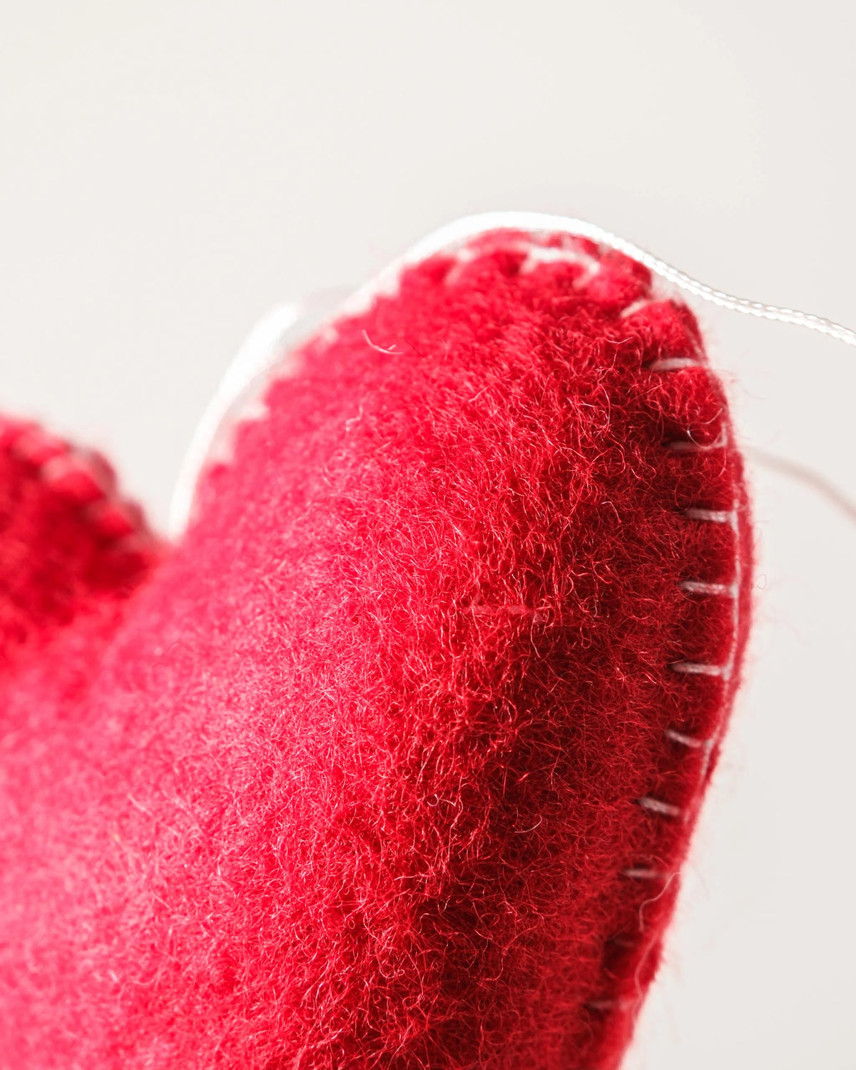 Grand coeur rouge a suspendre en feutrine sur un fond blanc détail zoom matière.