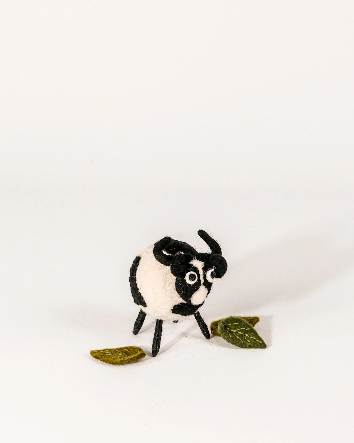 Petite vache noire en feutrine sur un fond blanc.
