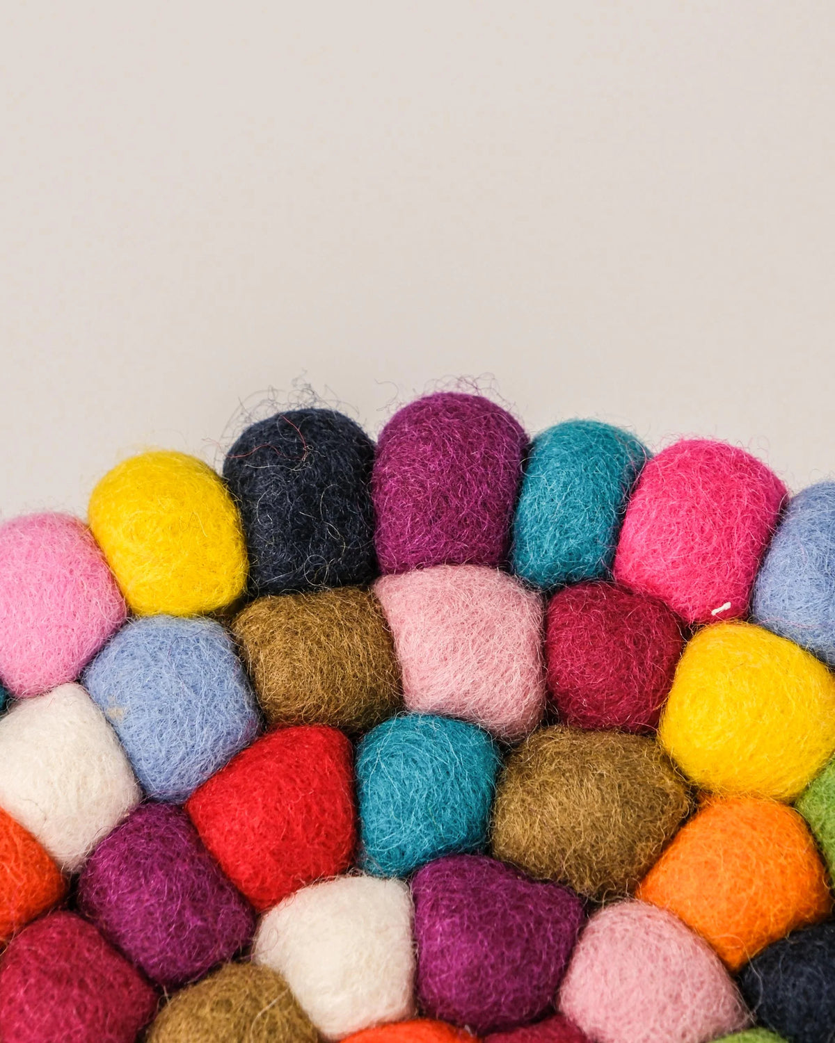 Dessous de plat boule en feutrine multicolore sur un fond blanc détail zoom matière.