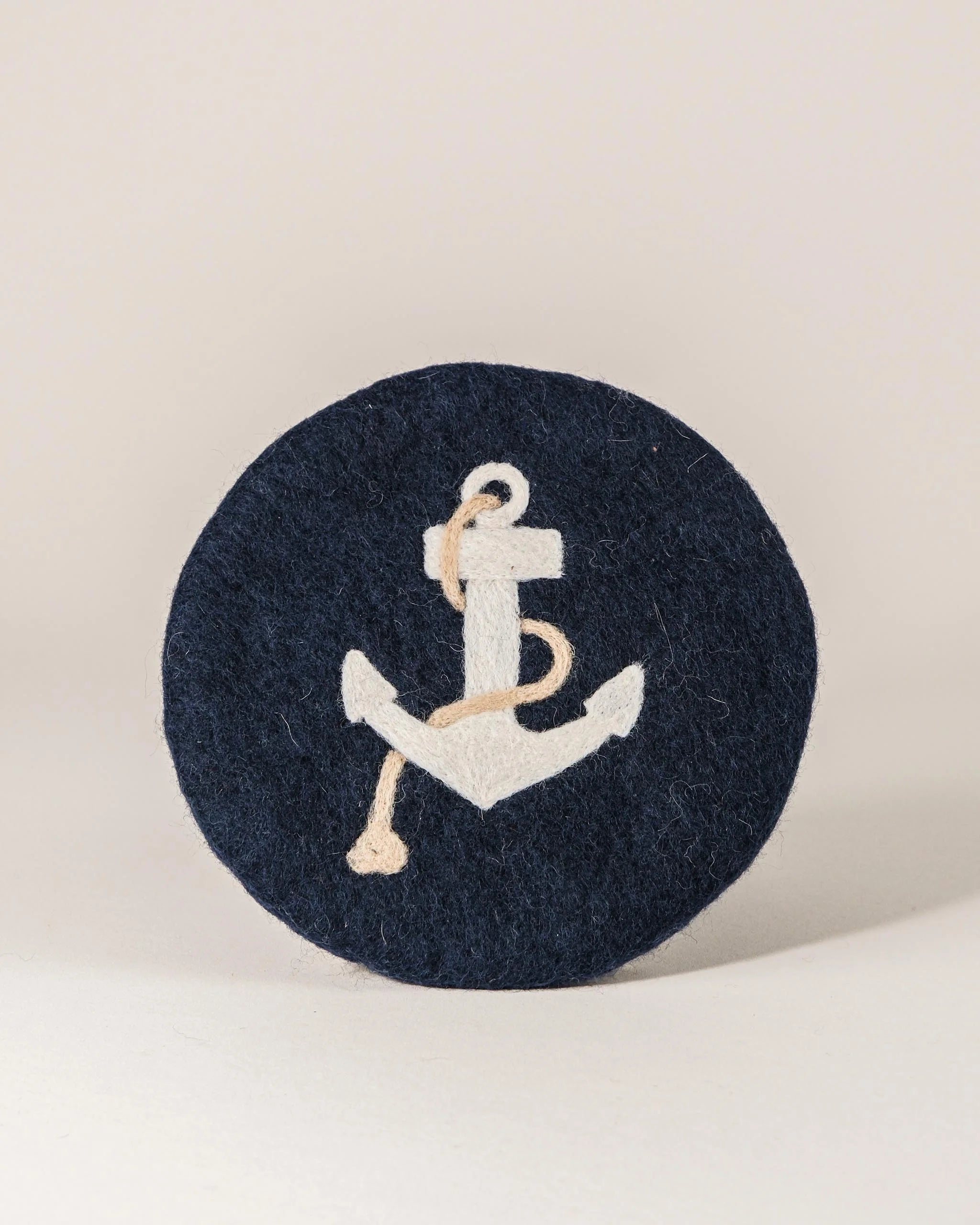 Dessous de plat boule en feutrine motif ancre sur un fond blanc.