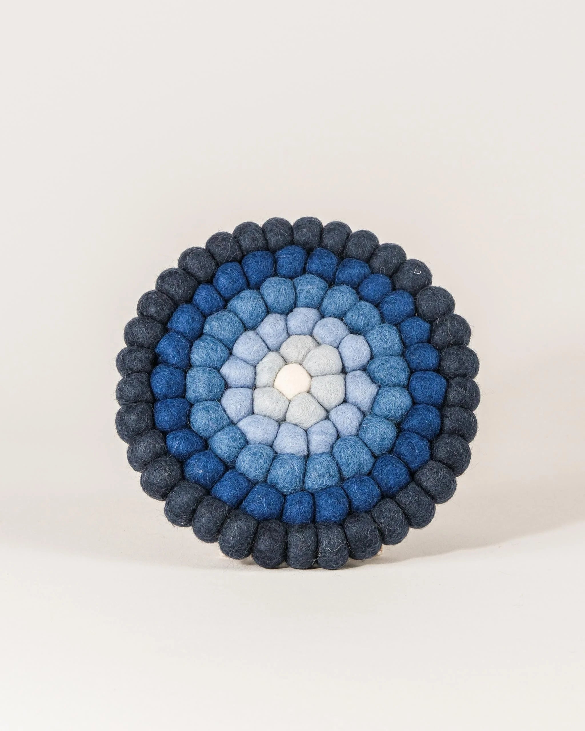 Dessous de plat boule dégradé de bleu en feutrine sur un fond blanc.