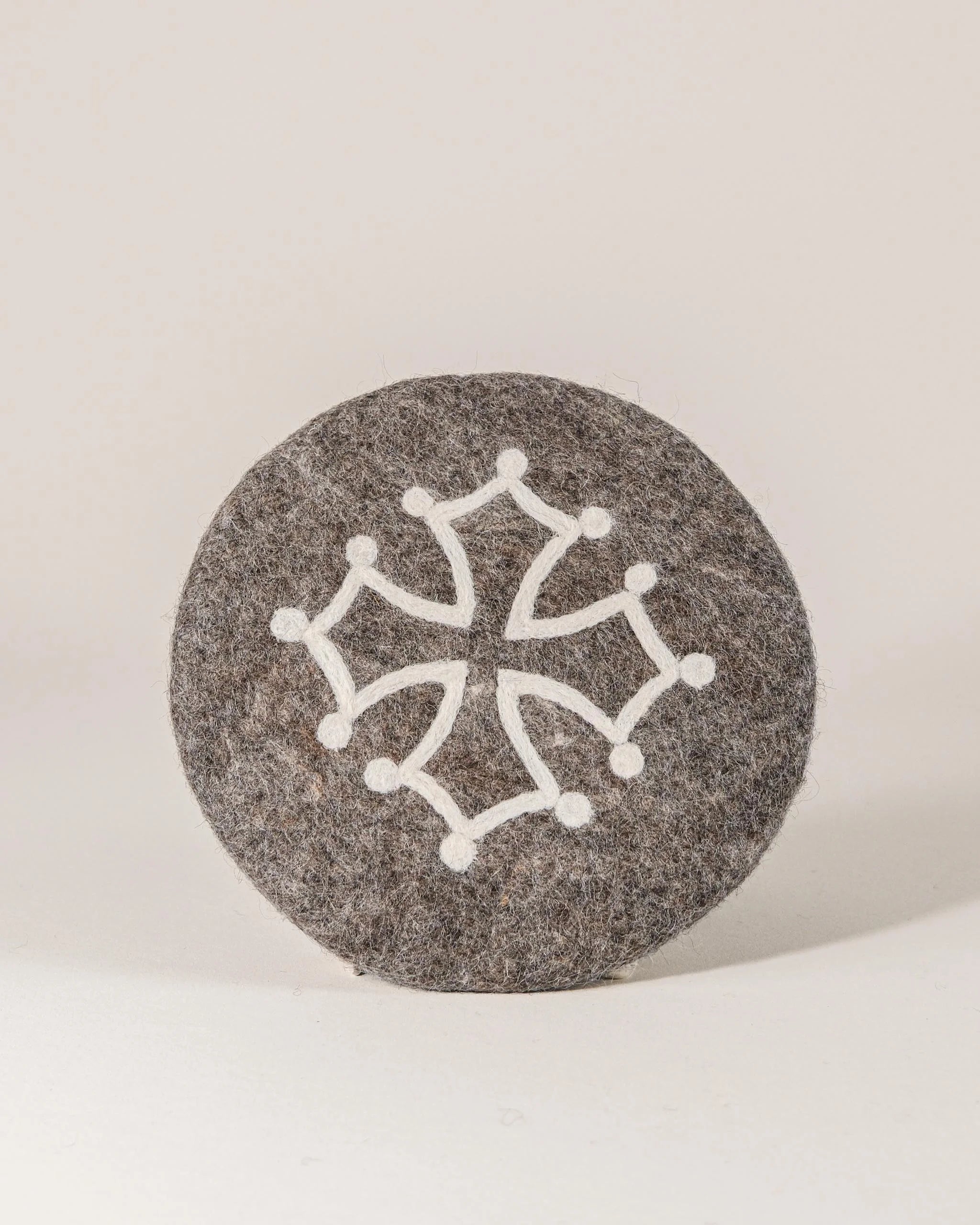 Dessous de plat boule en feutrine motif croix occitane sur un fond blanc.