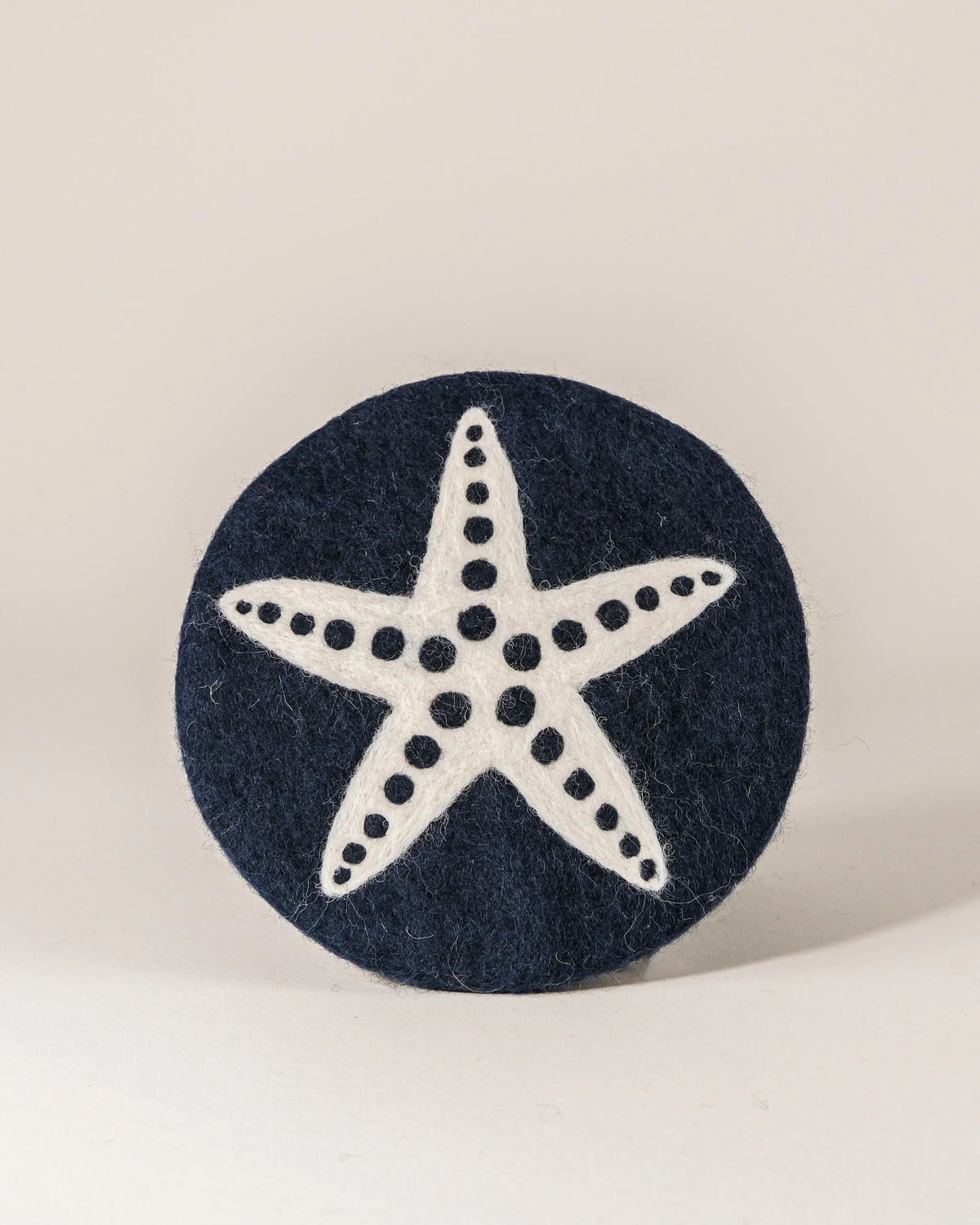 Dessous de plat boule en feutrine motif étoile de mer sur un fond blanc.