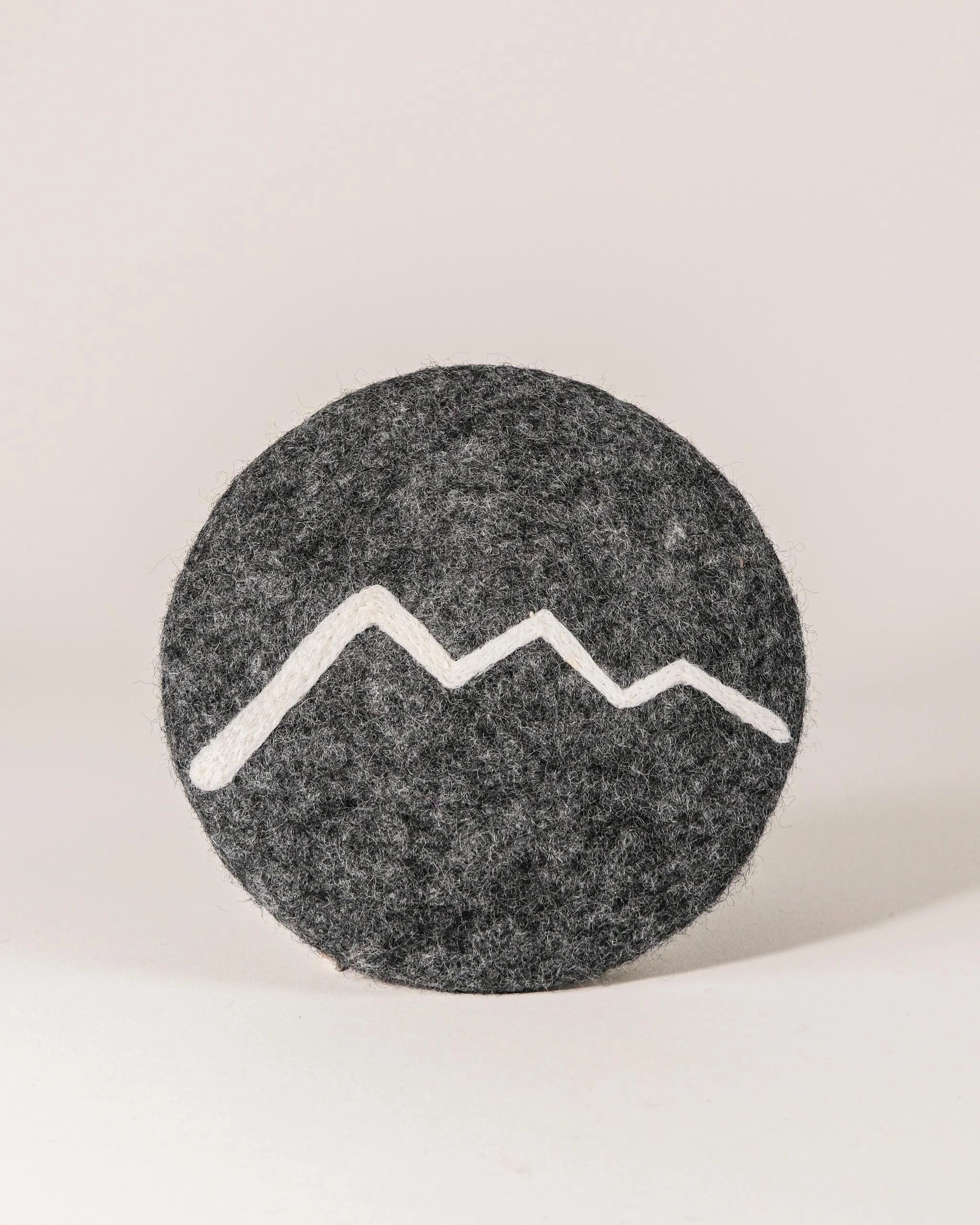 Dessous de plat boule en feutrine motif montagne sur un fond blanc.