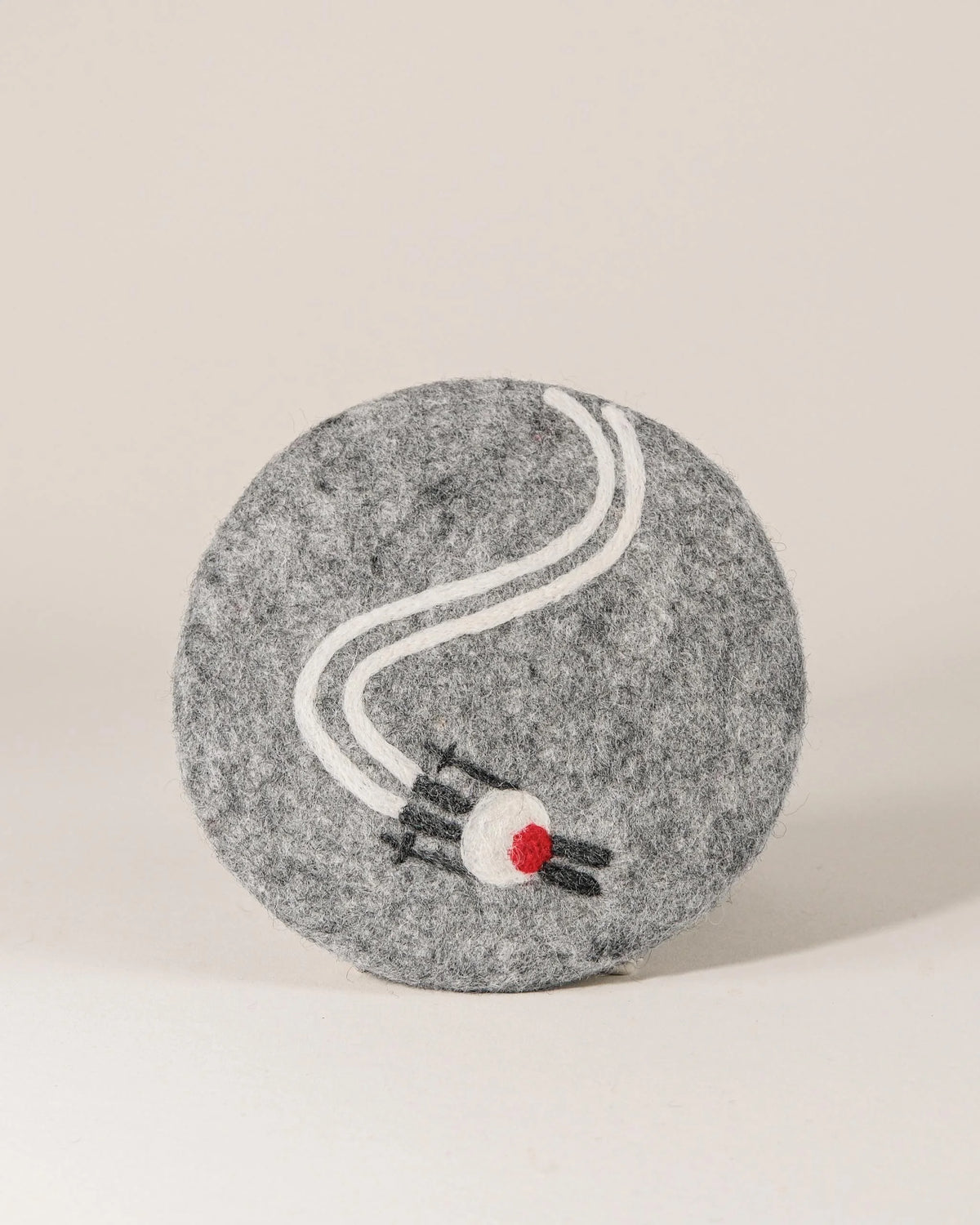 Dessous de plat boule en feutrine motif ski sur un fond blanc.