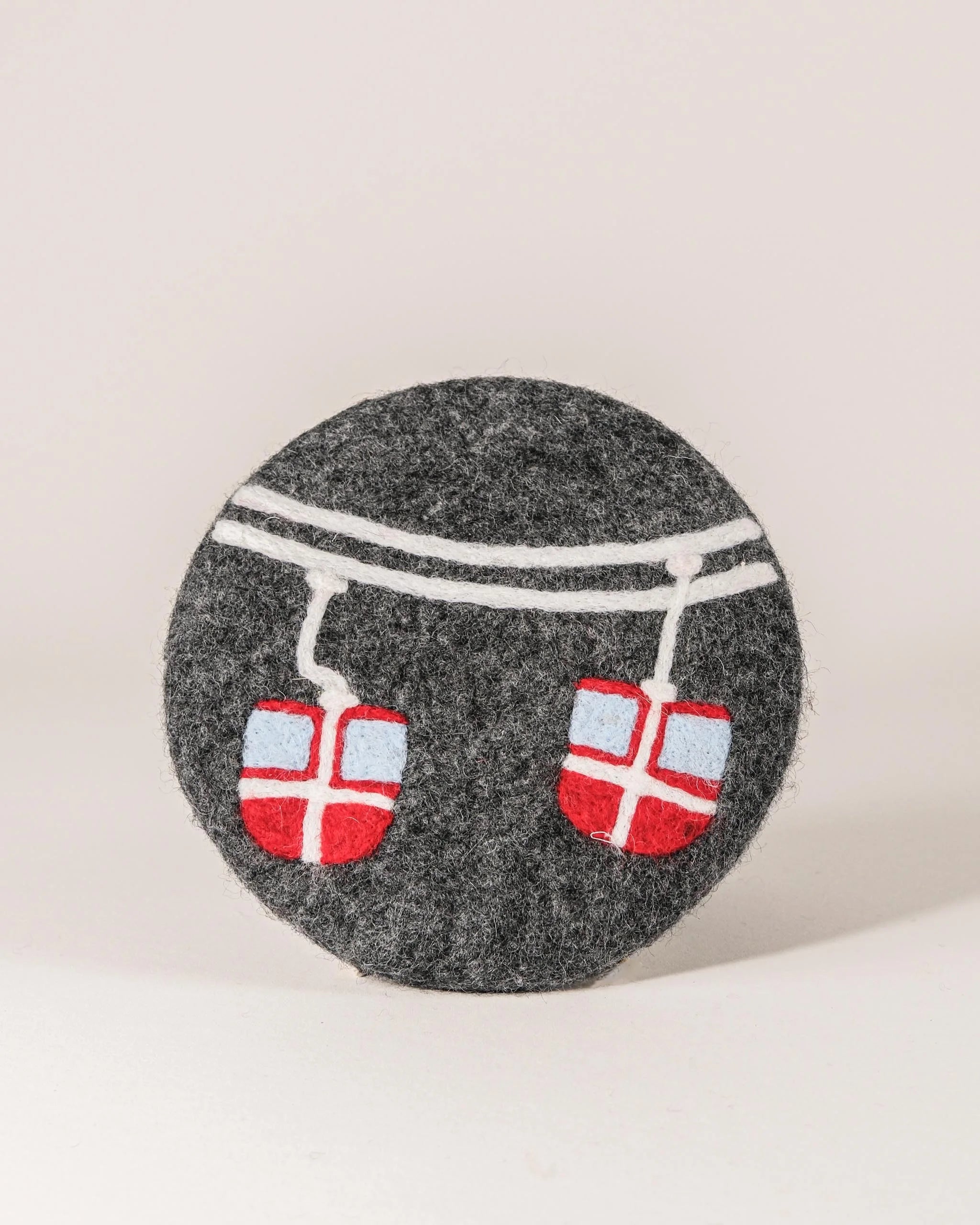 Dessous de plat boule en feutrine motif télécabine sur un fond blanc.