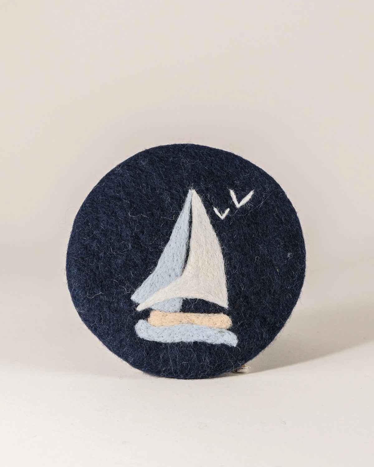 Dessous de plat boule en feutrine motif voilier sur un fond blanc.
