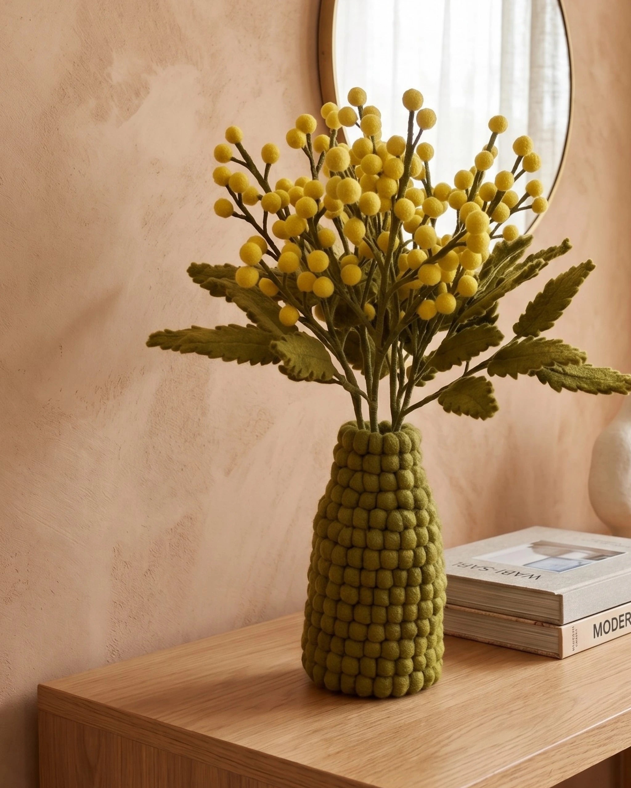 Bouquet de mimosa en feutrine dans un vase en feutrine kaki posé sur une table en bois.