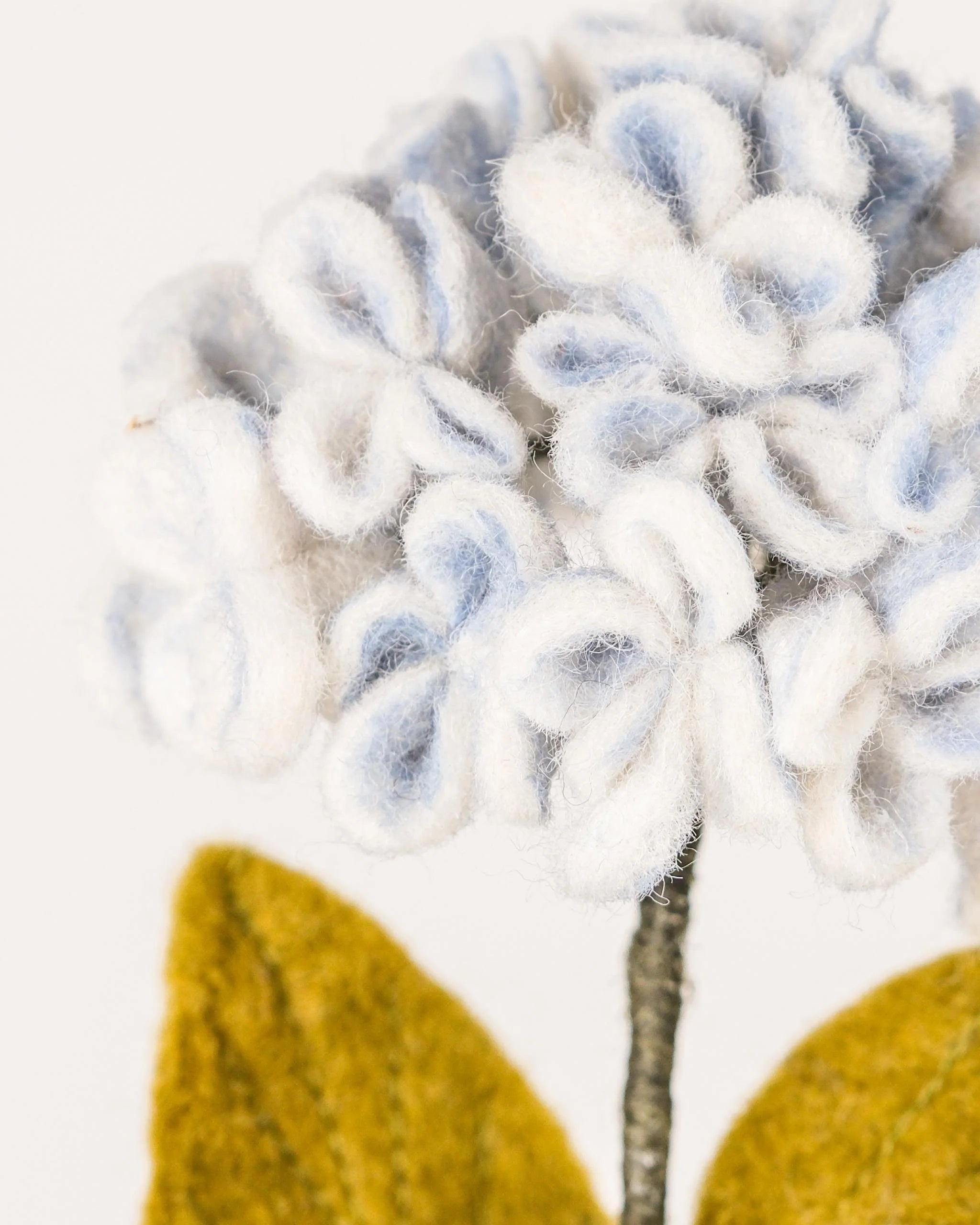 Photo zoom d'une hortensia bleu en feutrine sur un fond blanc.