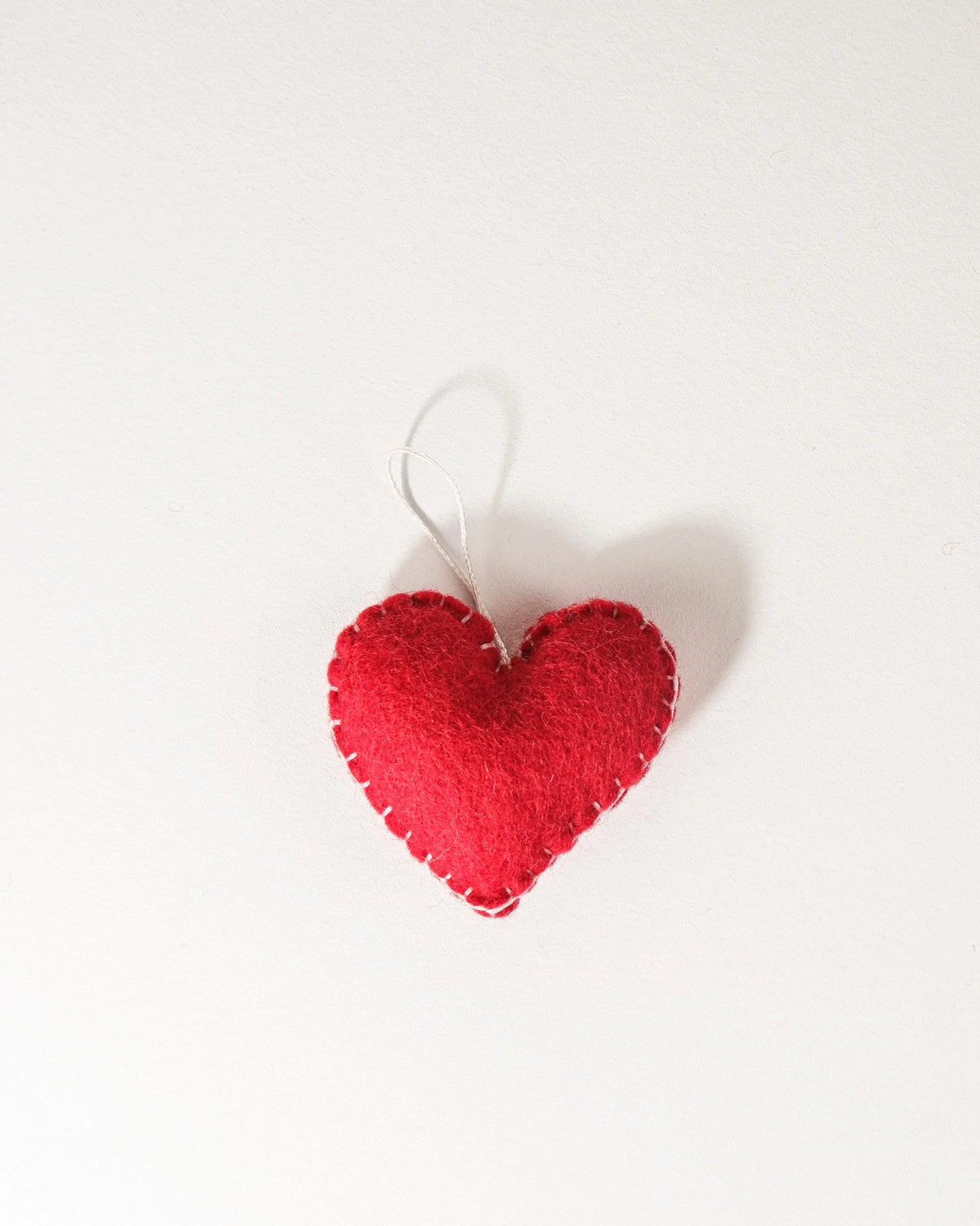 Grand coeur rouge a suspendre en feutrine sur un fond blanc.