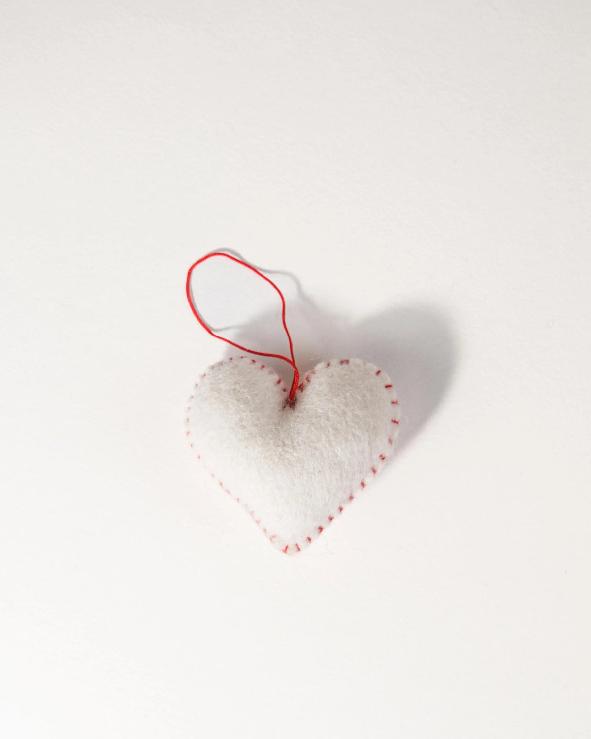 Mini coeur blanc a suspendre en feutrine sur un fond blanc.