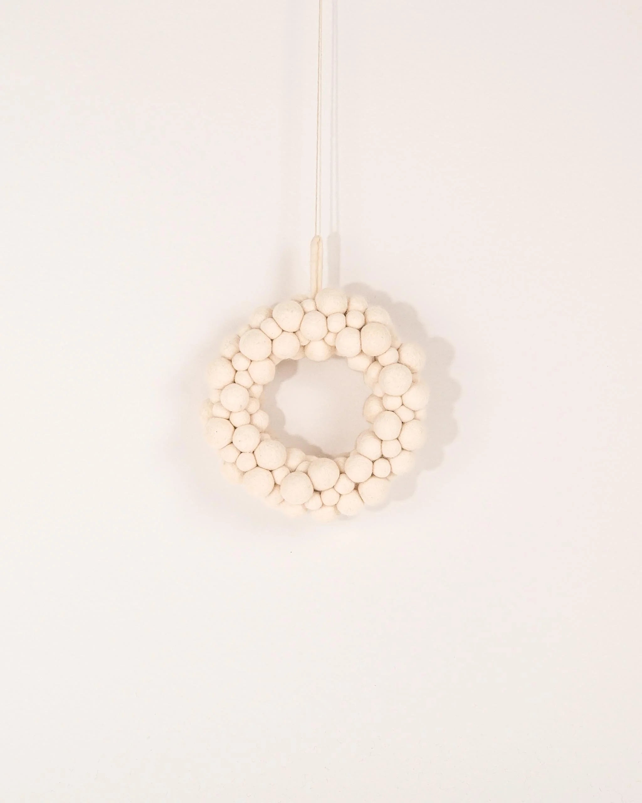 Couronne en feutrine boules blanche sur un mur blanc.