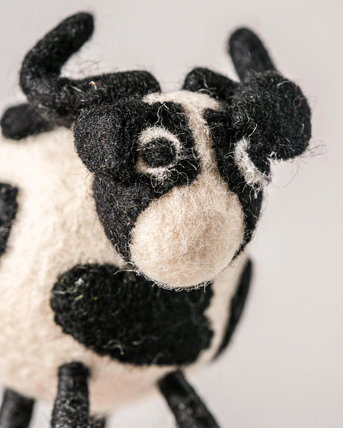 Petite vache noire en feutrine sur un fond blanc détail zoom matière.