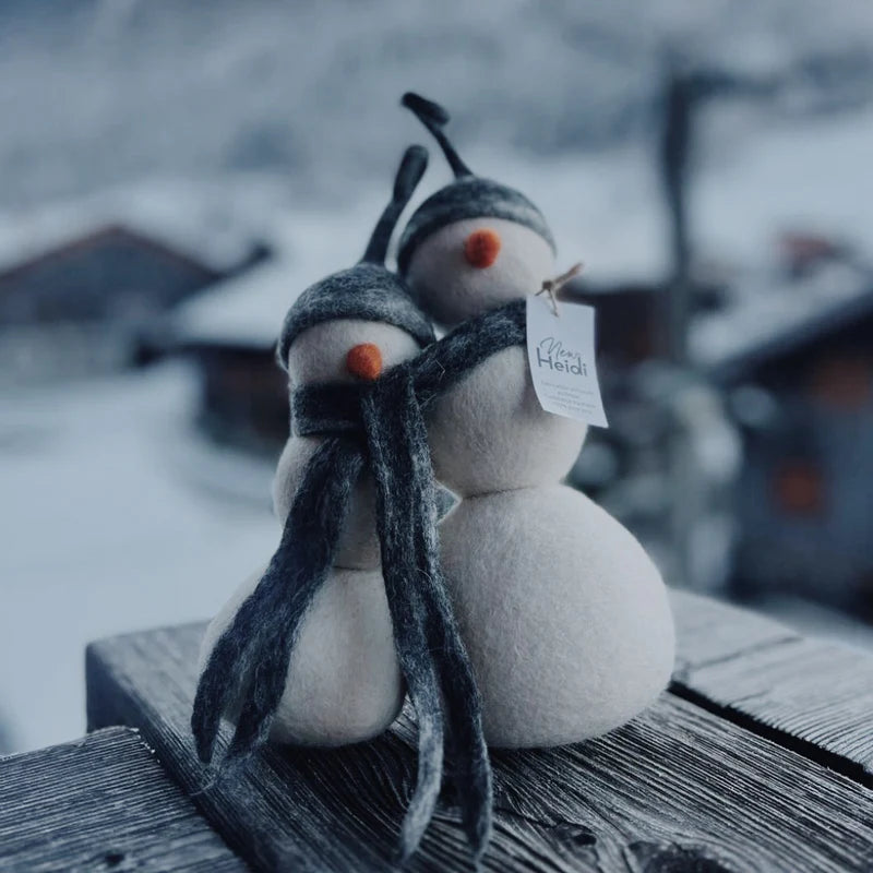 Duo de bonshommes de neige New Heidi en laine feutrée blanche avec bonnets et écharpe gris sur un balcon de montagne.