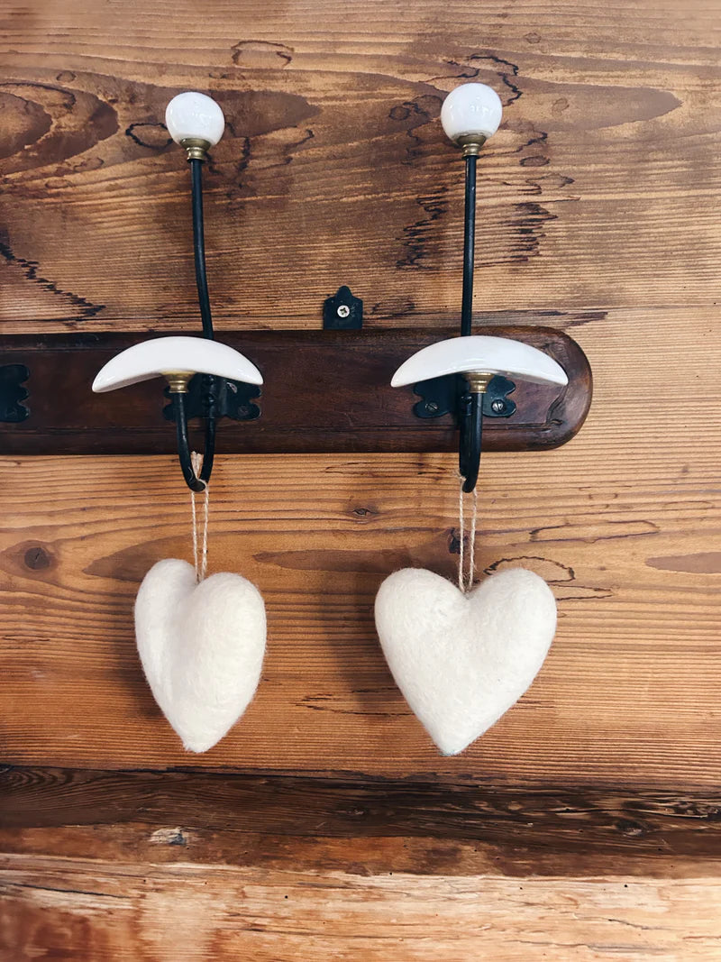 Deux cœurs en laine feutrée New Heidi suspendus à un porte-manteau rustique en bois.