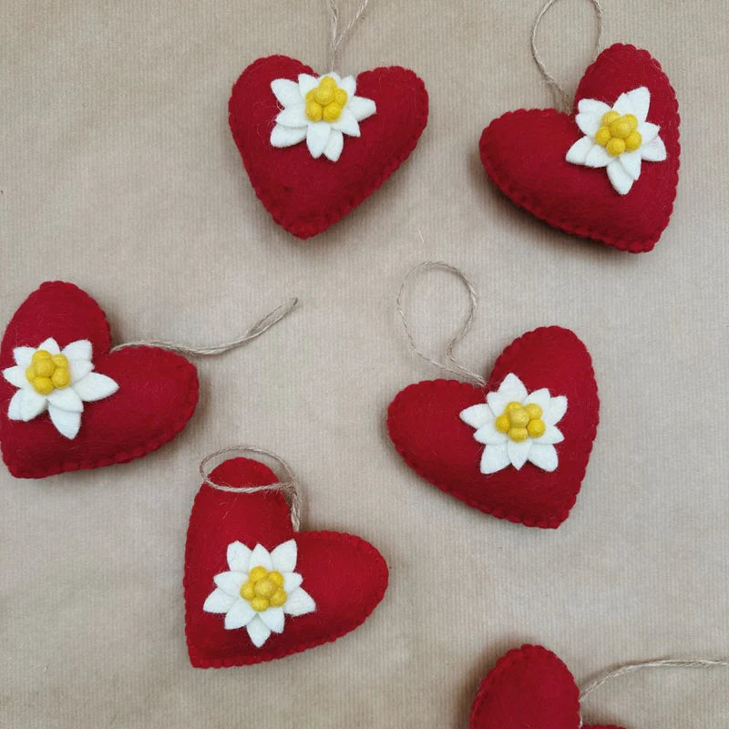 Plusieurs cœurs en feutrine rouge ornés d'edelweiss disposés pour une décoration de Noël chaleureuse.