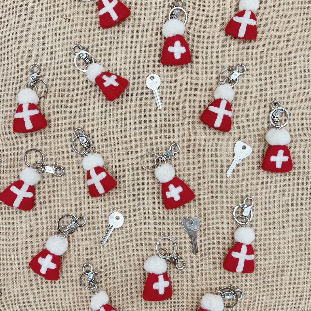 Accumulation de porte-clés régionaux en laine feutrée en forme de bonnets savoyards rouges et blancs parsemés sur une toile de jute.