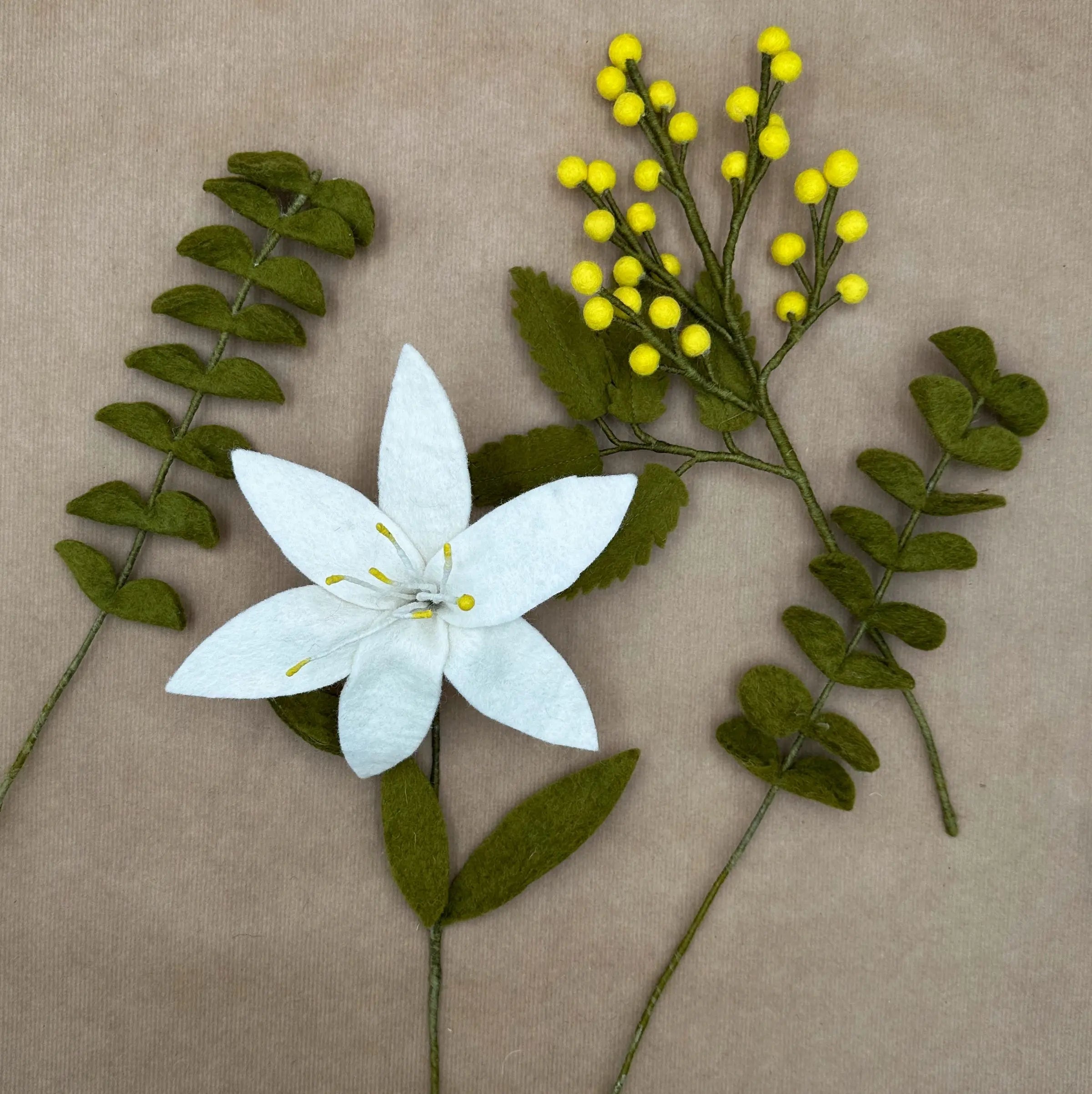 Présentation des quatre tiges artisanales (lys, mimosa et eucalyptus) du bouquet Pureté de Printemps.