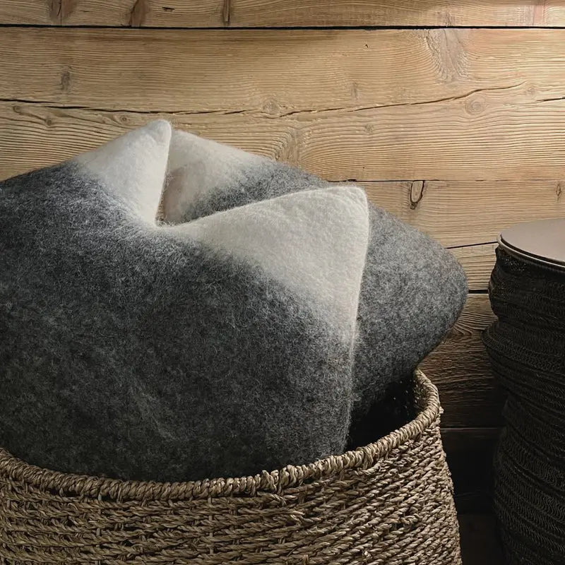 Coussin montagne simple New Heidi en feutrine grise et blanche dans un panier en osier.