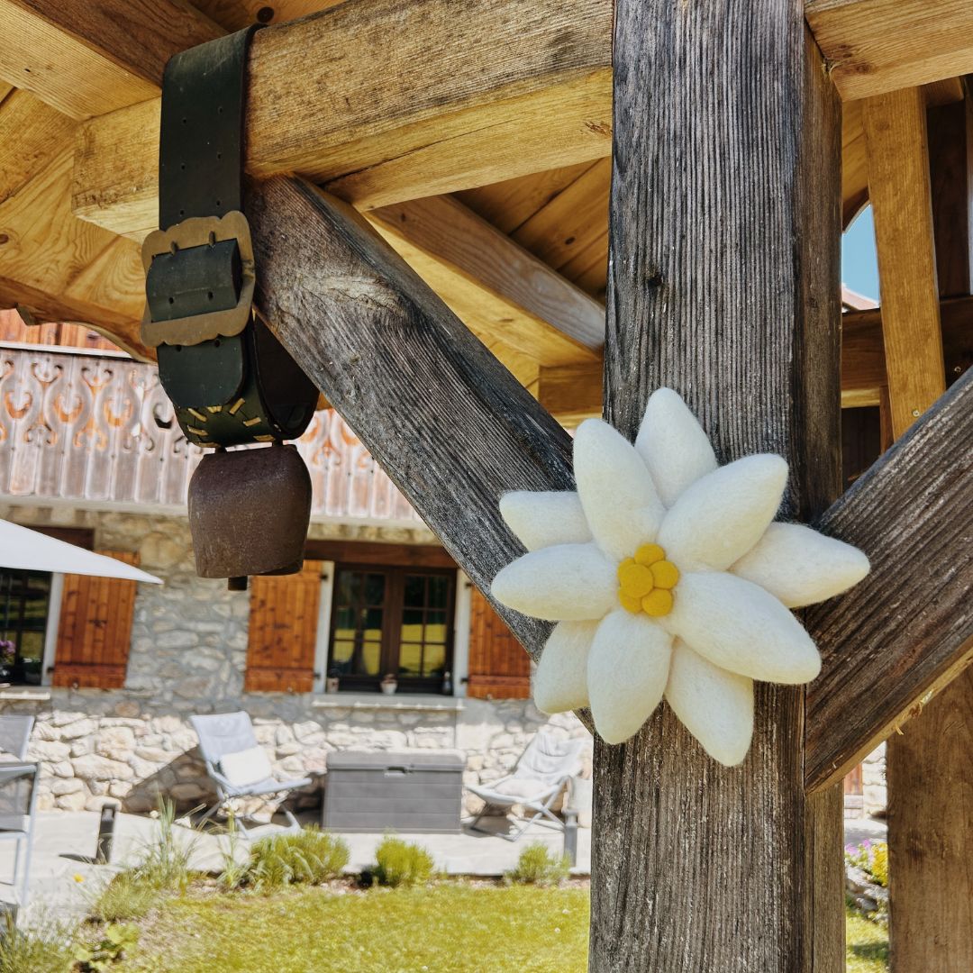 Fleur d'edelweiss en feutrine blanche suspendue à un poteau de terrasse en bois avec une cloche de vache traditionnelle.