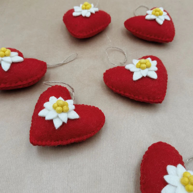 Plusieurs cœurs en feutrine rouge ornés d'edelweiss disposés pour une décoration de Noël chaleureuse.