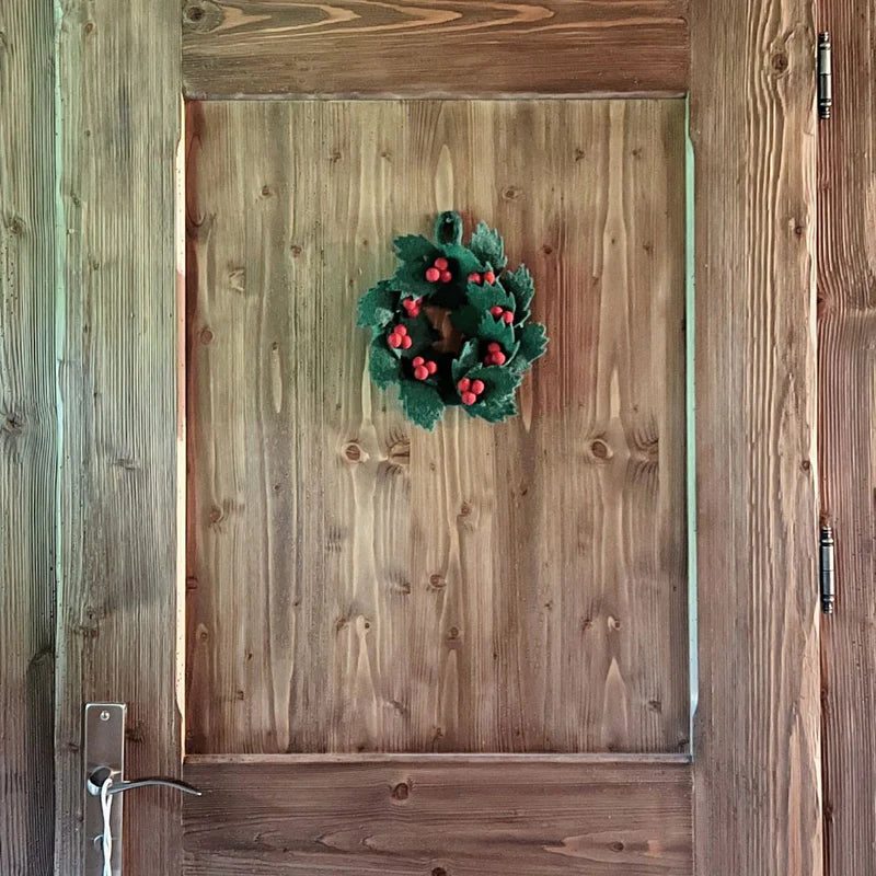 Couronne de houx artisanale New Heidi de 20 cm suspendue sur une porte en bois rustique.
