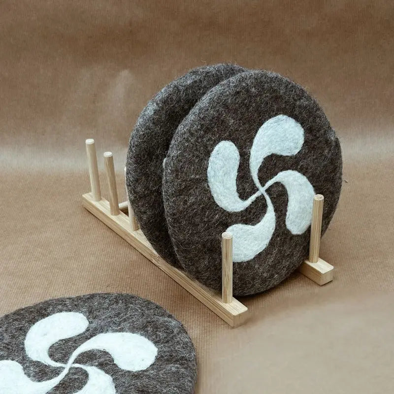 Dessous de plat artisanaux motif Croix Basque New Heidi présentés sur un support en bois.