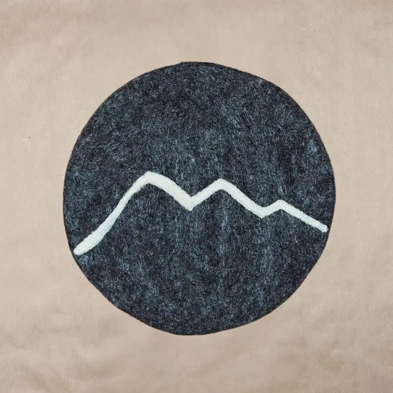 Dessous de plat rond en feutrine grise avec motif de montagnes blanc brodé artisanalement par New Heidi.