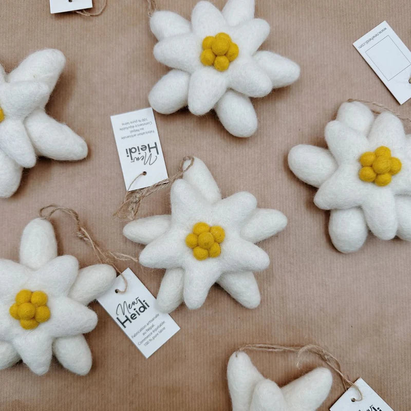 Groupe de fleurs d'edelweiss à suspendre New Heidi en laine blanche et jaune sur fond kraft.