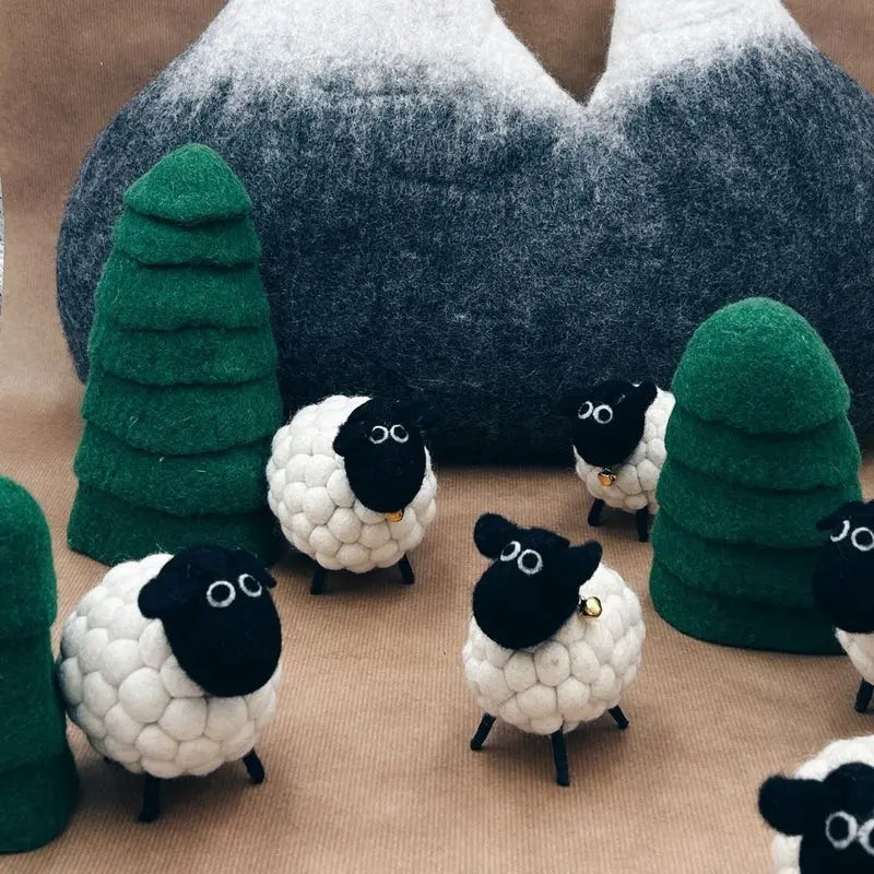 Mise en scène de moutons têtes noires New Heidi dans un paysage de montagne avec sapins en laine.