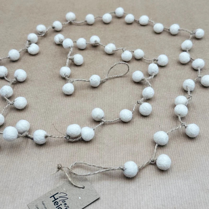 Guirlande décorative New Heidi composée de billes en laine feutrée blanche sur ficelle naturelle.