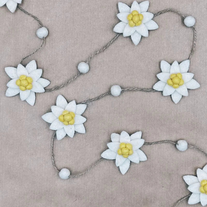 Guirlande décorative New Heidi composée de fleurs d'edelweiss et de billes en laine feutrée sur fond kraft.