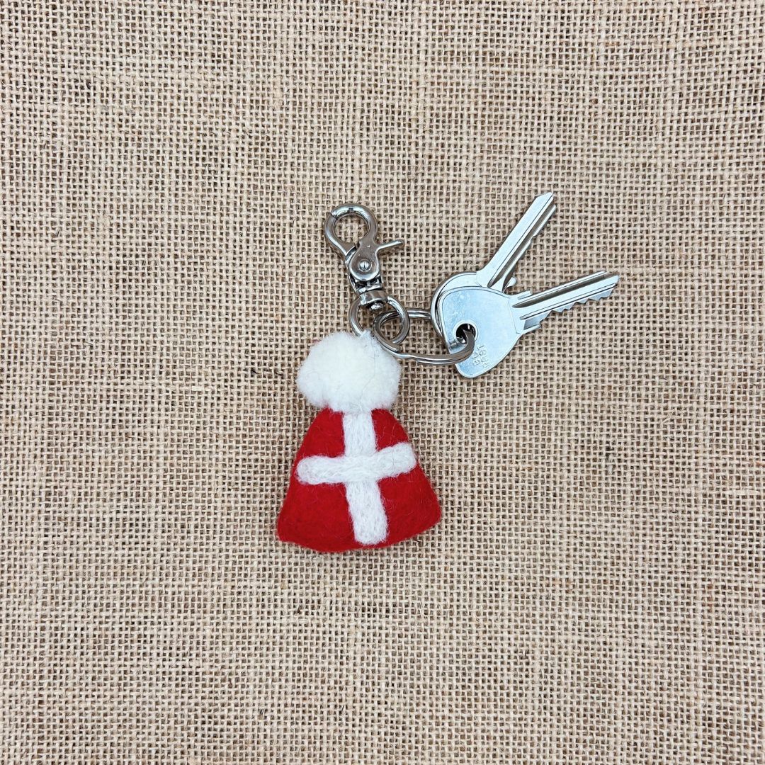 Porte-clé en feutrine rouge New Heidi en forme de bonnet savoyard avec croix blanche et pompon accroché à des clés.