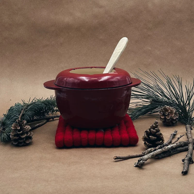 Poêlon à raclette posé sur le dessous de plat drapeau savoyard New Heidi, ambiance bois.