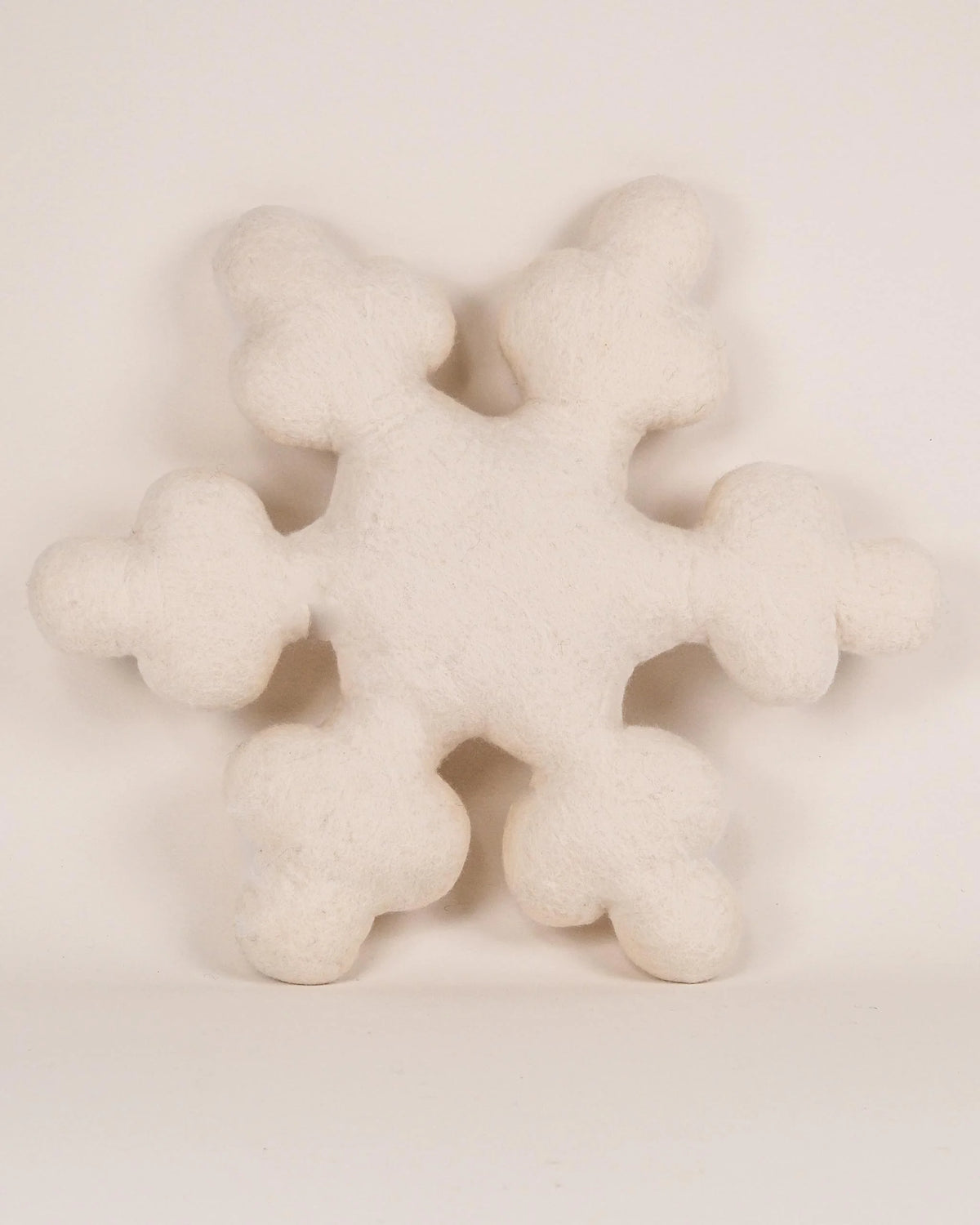 Coussin décoratif flocon en feutrine sur fond blanc.