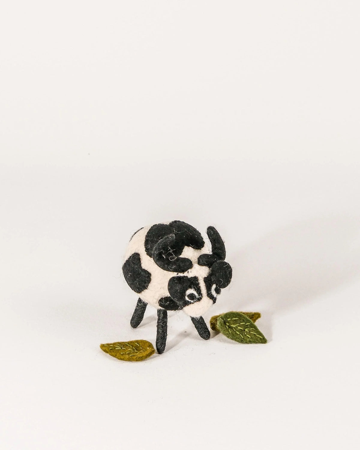 Grande vache noire en feutrine sur un fond blanc.