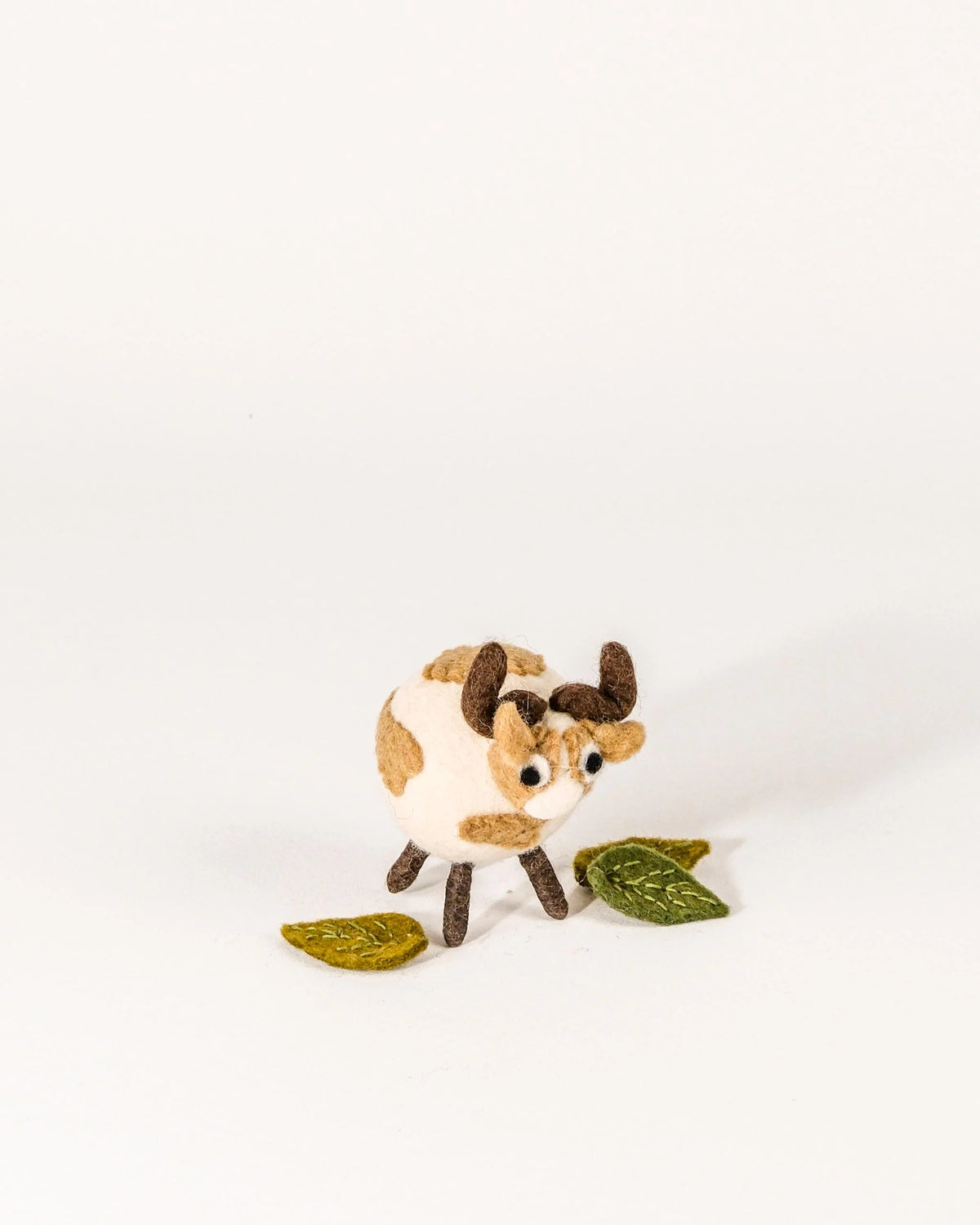 Petite vache marron en feutrine sur un fond blanc.