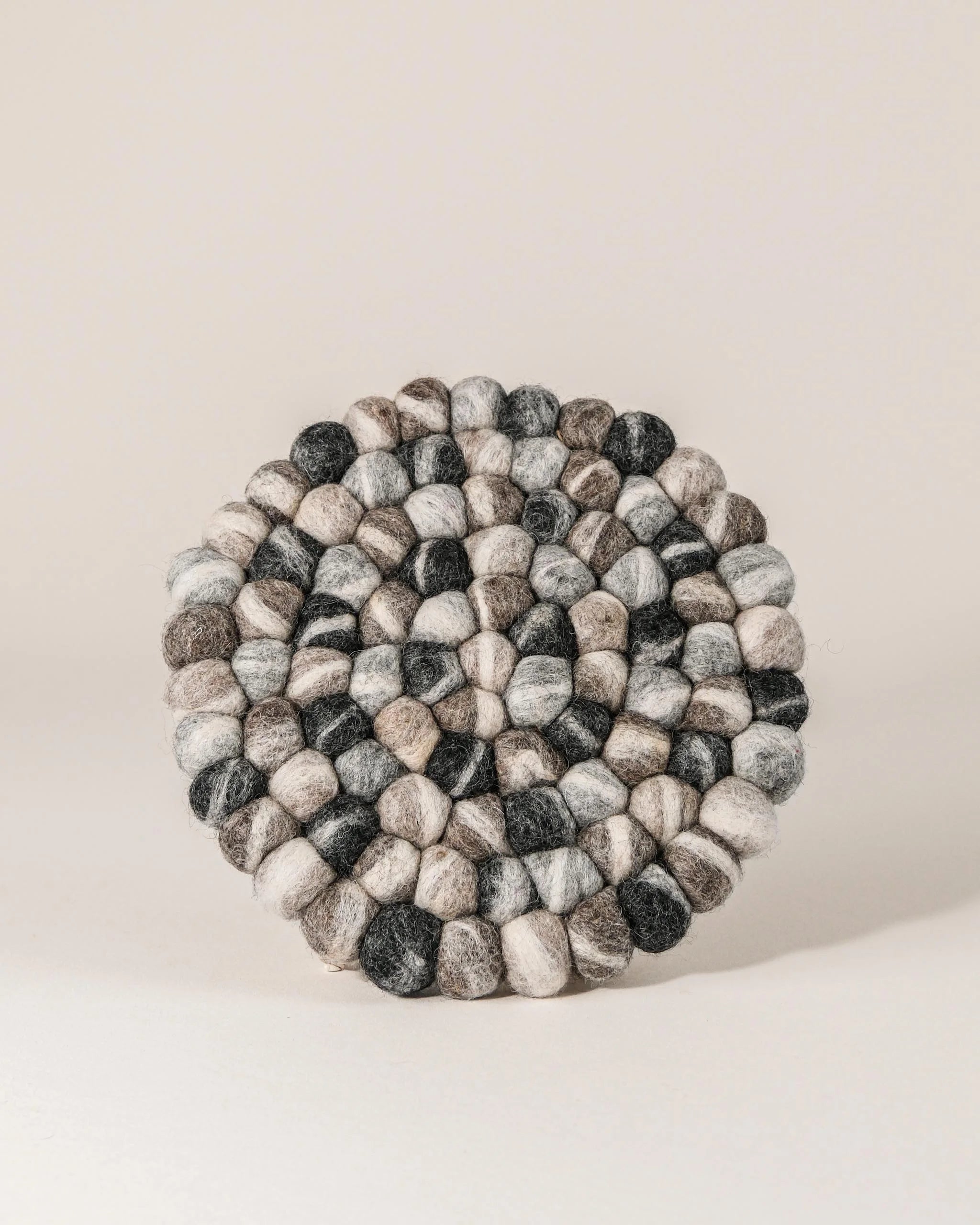 Dessous de plat boule en feutrine galet sur un fond blanc.