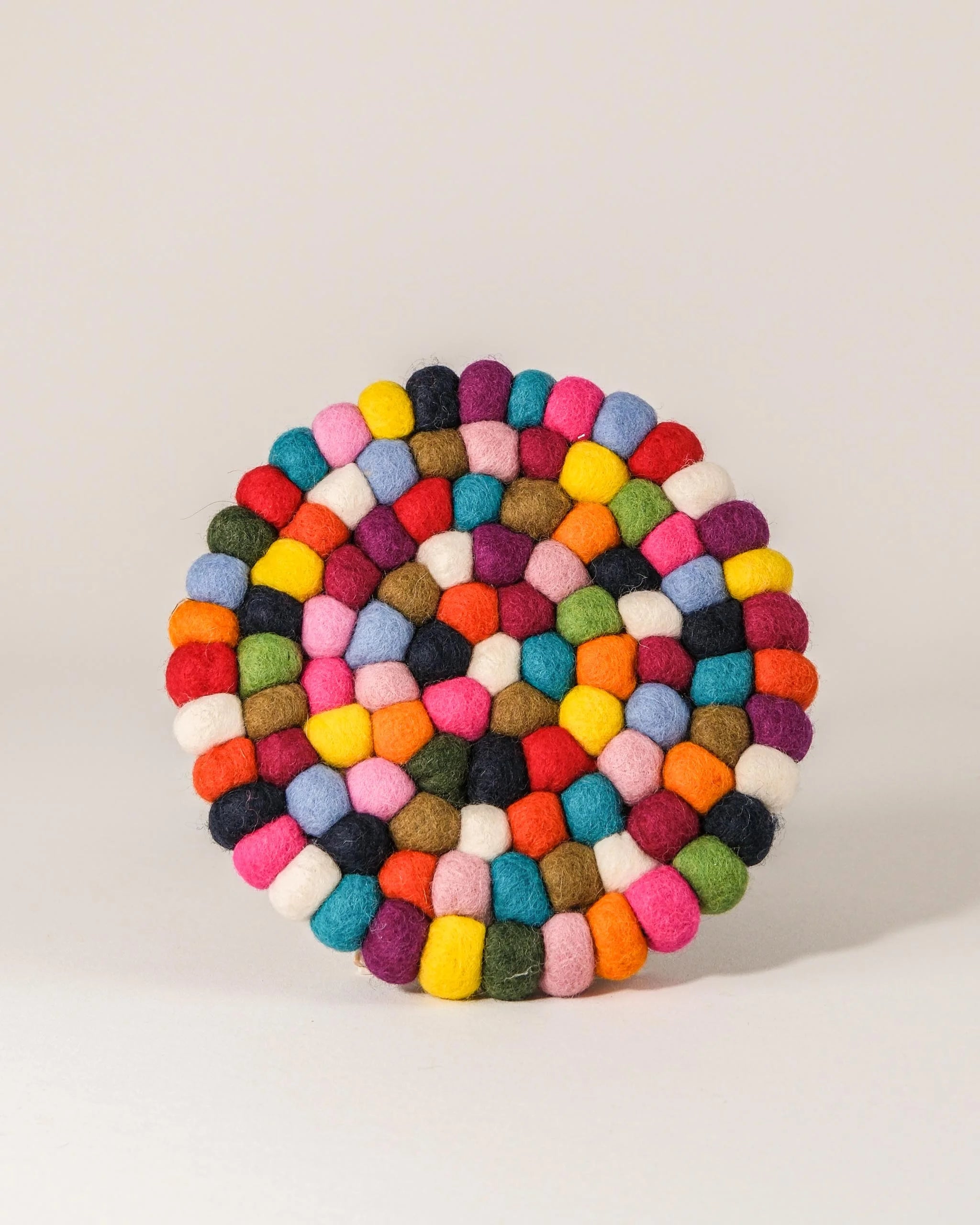 Dessous de plat boule en feutrine multicolore sur un fond blanc.