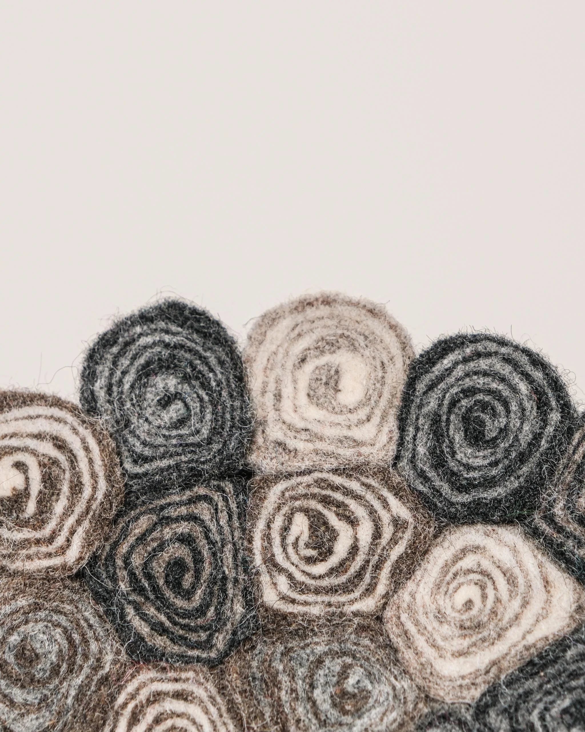 Dessous de plat boule en feutrine spirale sur un fond blanc détail zoom matière.