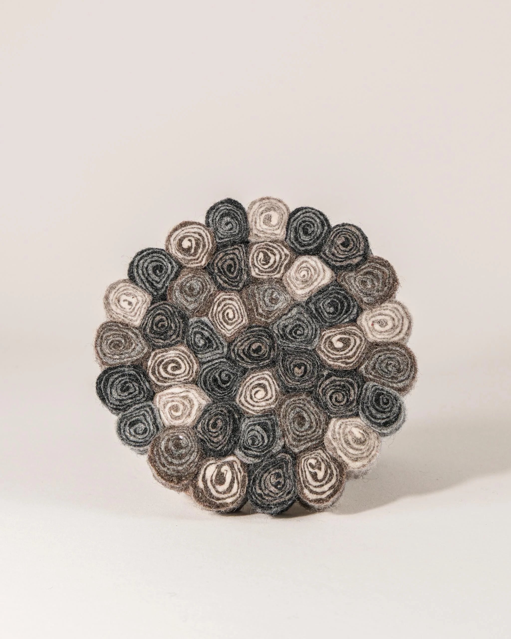 Dessous de plat boule en feutrine spirale sur un fond blanc.