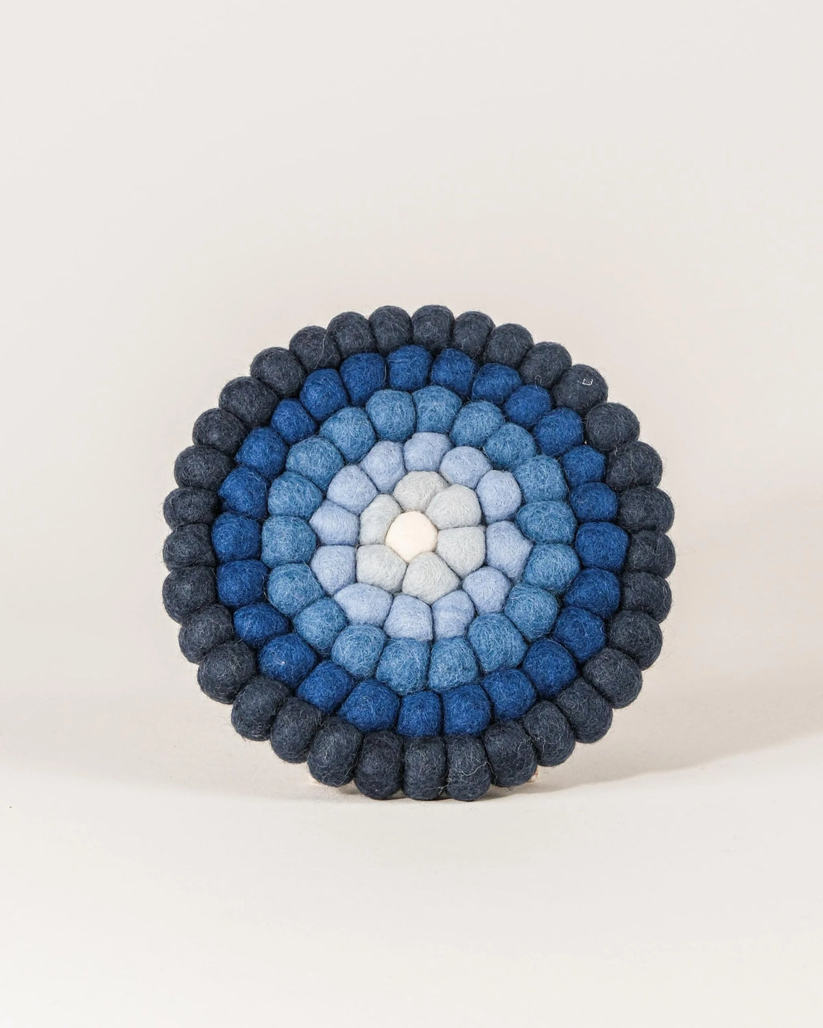 Dessous de plat boule dégradé de bleu en feutrine sur un fond blanc.