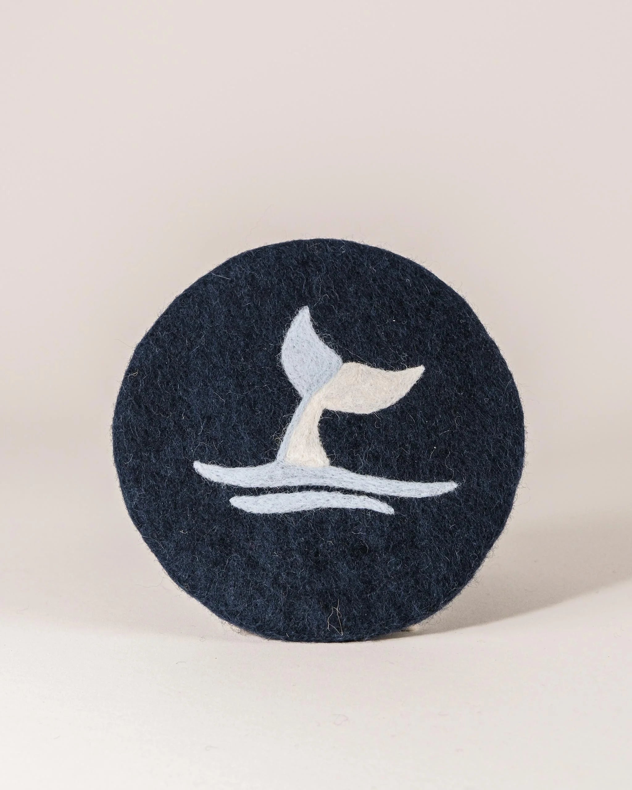 Dessous de plat boule en feutrine motif baleine sur un fond blanc.