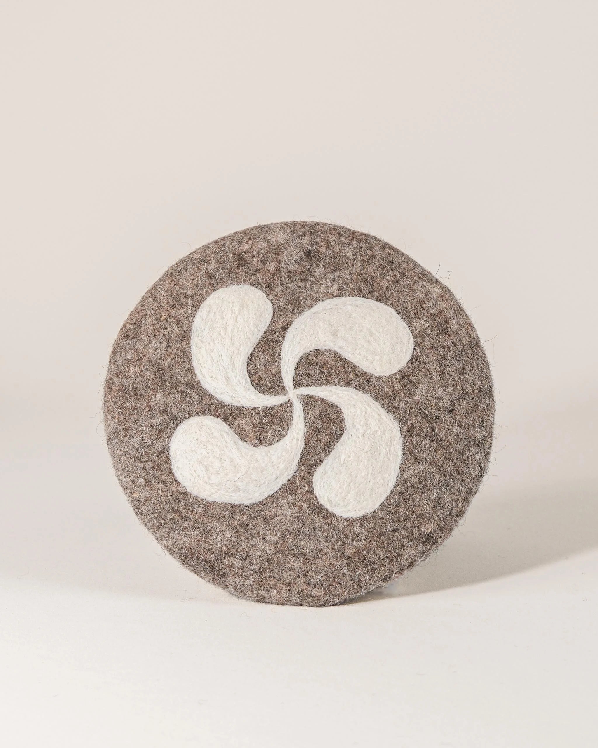 Dessous de plat boule en feutrine motif croix basque sur un fond blanc.