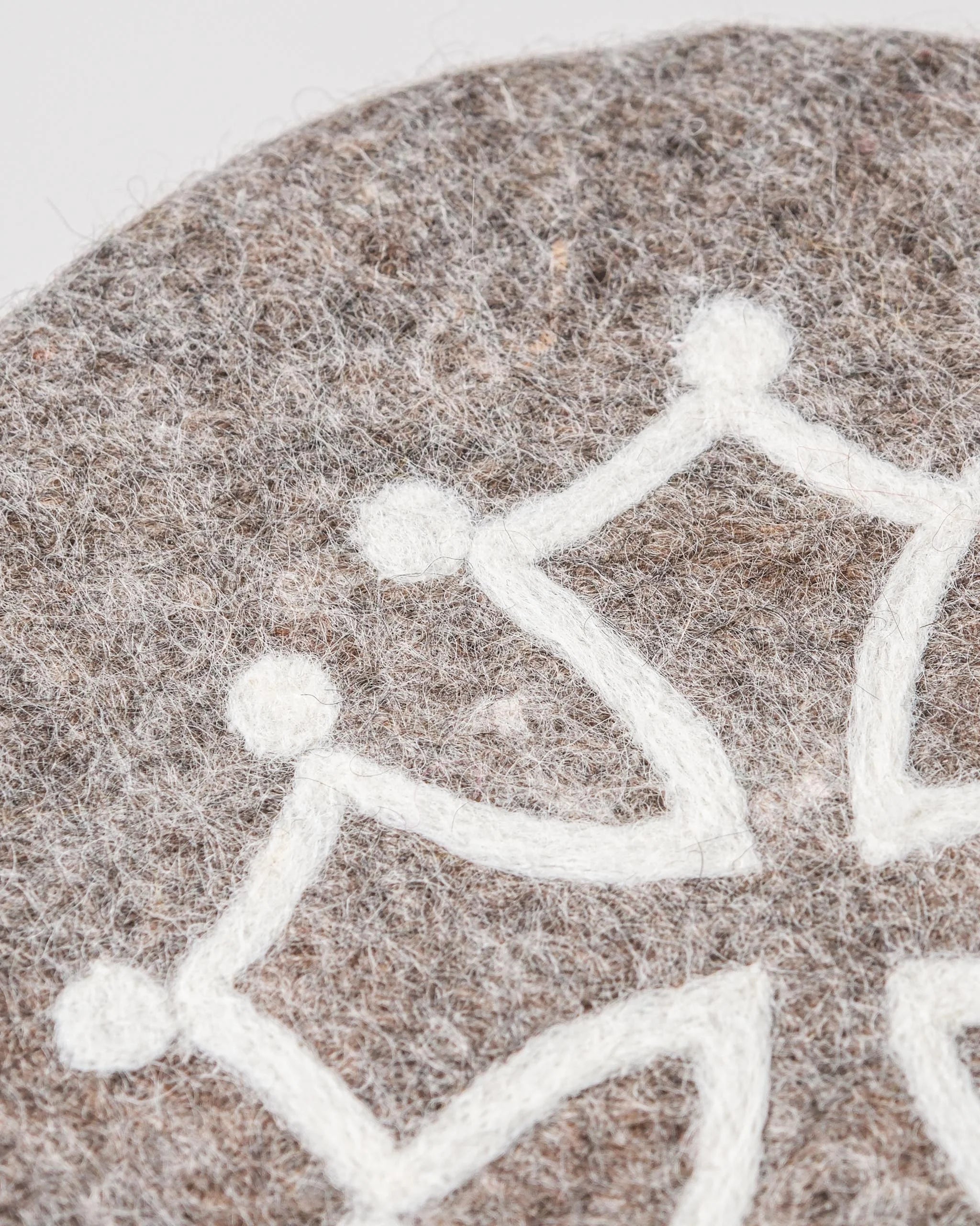 Dessous de plat boule en feutrine motif croix occitane sur un fond blanc détail zoom matière.