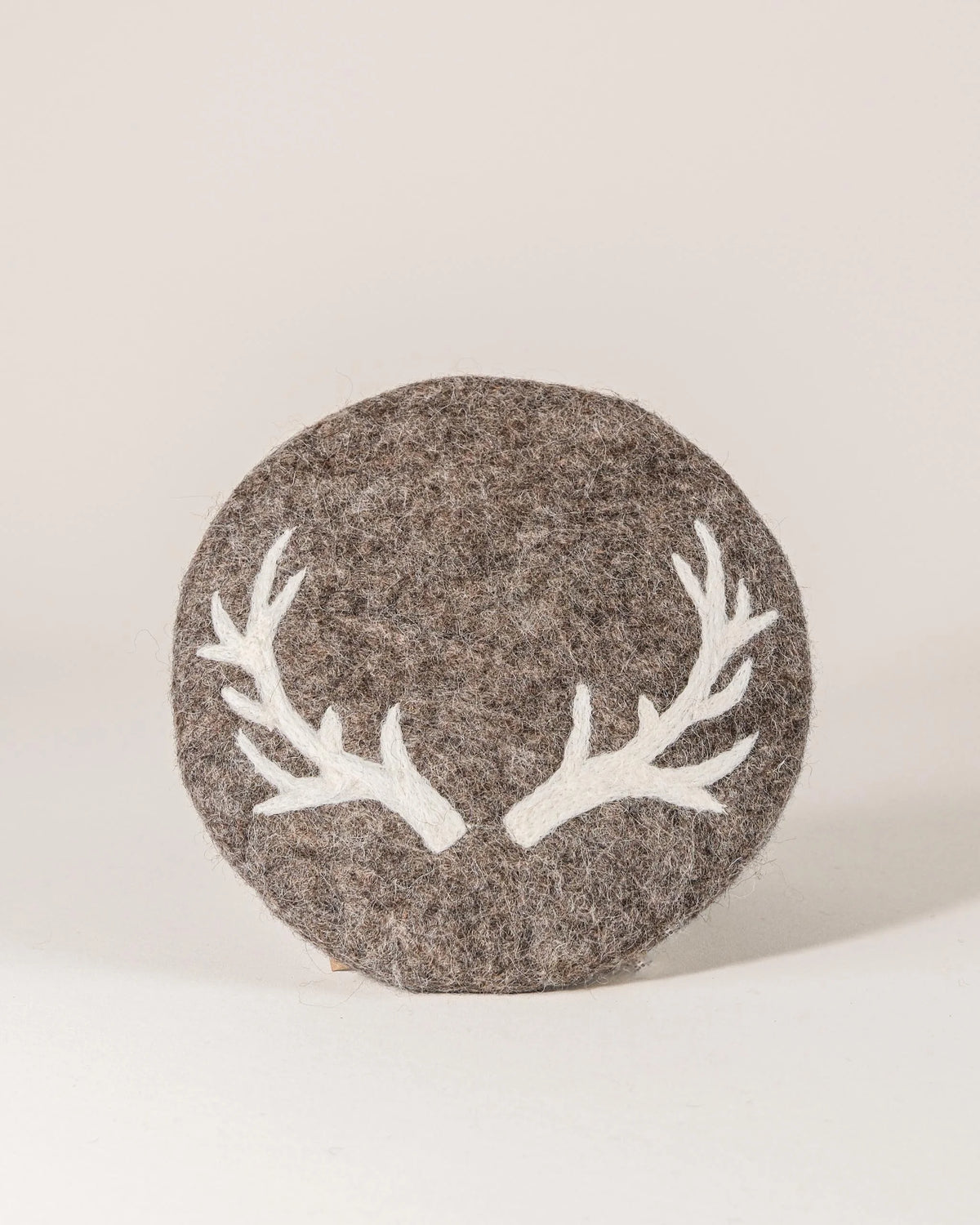 Dessous de plat boule en feutrine motif cerf sur un fond blanc.