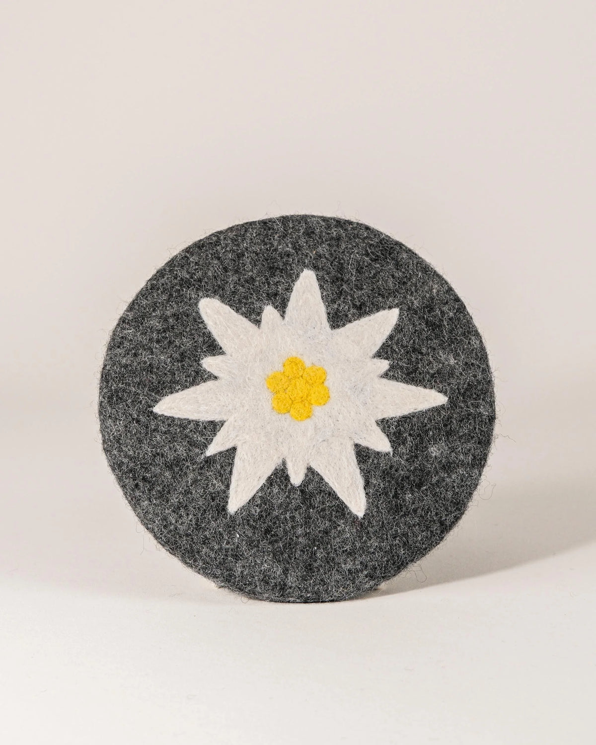 Dessous de plat boule en feutrine motif Edelweiss sur un fond blanc.
