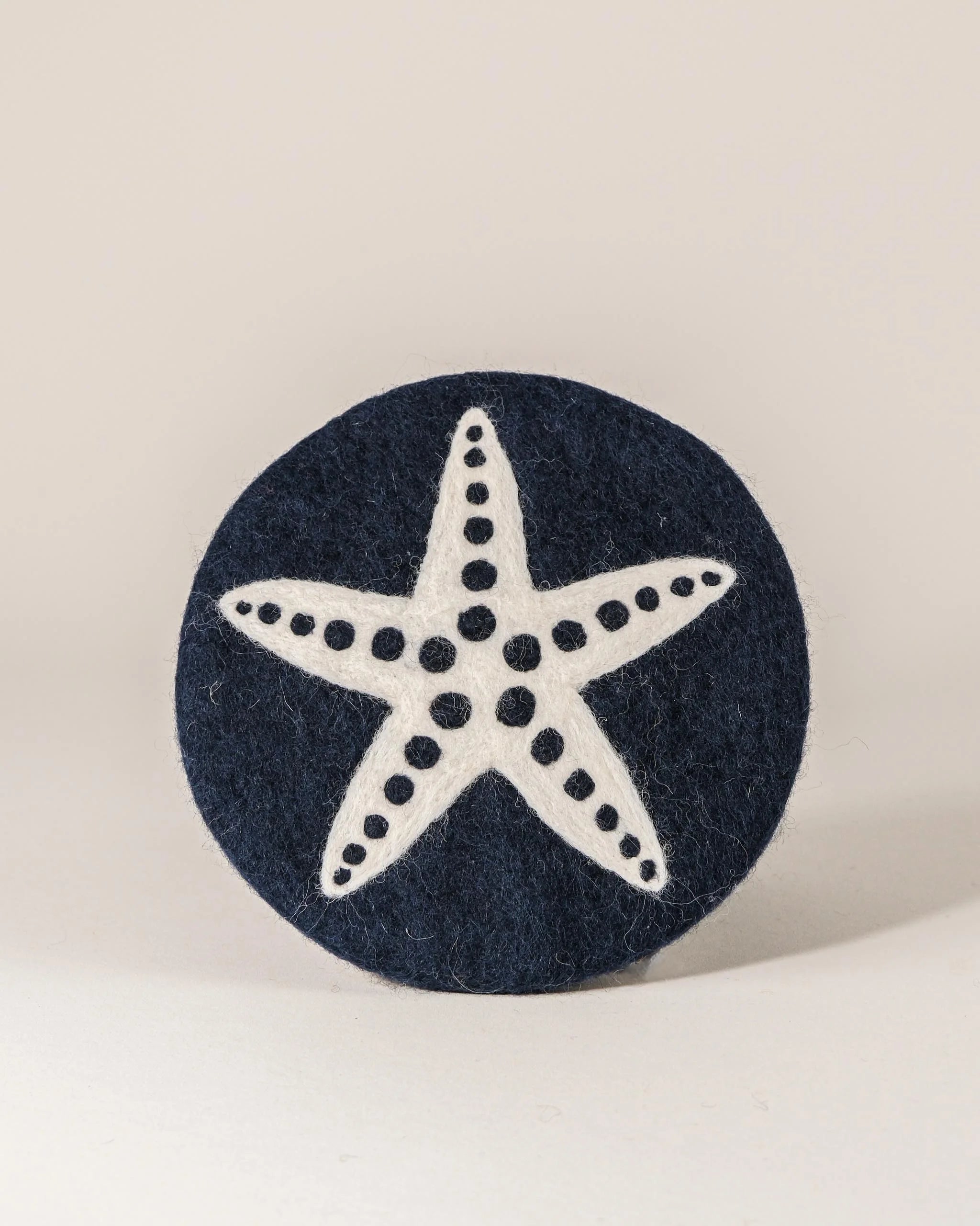 Dessous de plat boule en feutrine motif étoile de mer sur un fond blanc.